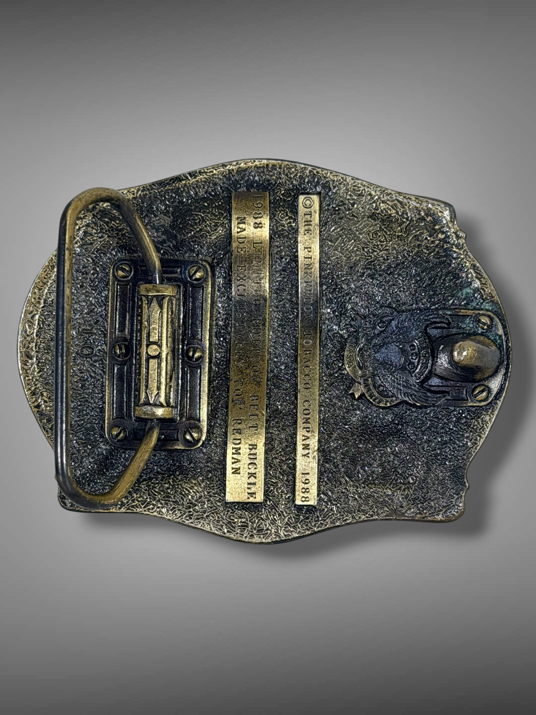 Back view of a Brass Monkey Vintage 1988 Red Man belt buckle featuring antique brass-tone metal and hook attachment.