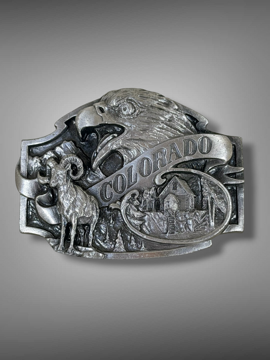 Brass Monkey Vintage 1988 Colorado metal belt buckle featuring a bald eagle, bighorn sheep, and mountain cabin relief.